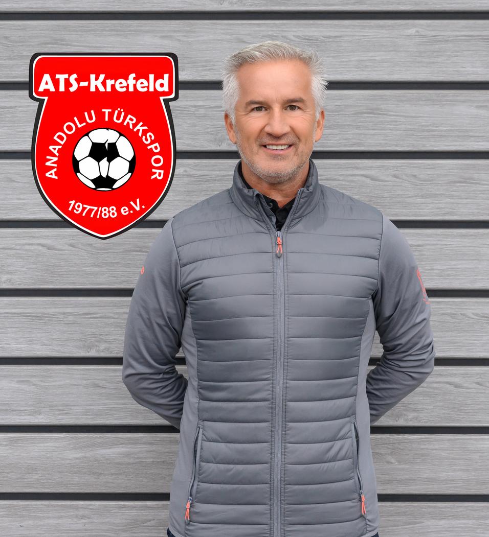 Mann in grauer Jacke steht vor einer grauen Wand, neben dem Logo von ATS Krefeld Anadolu Türksport.