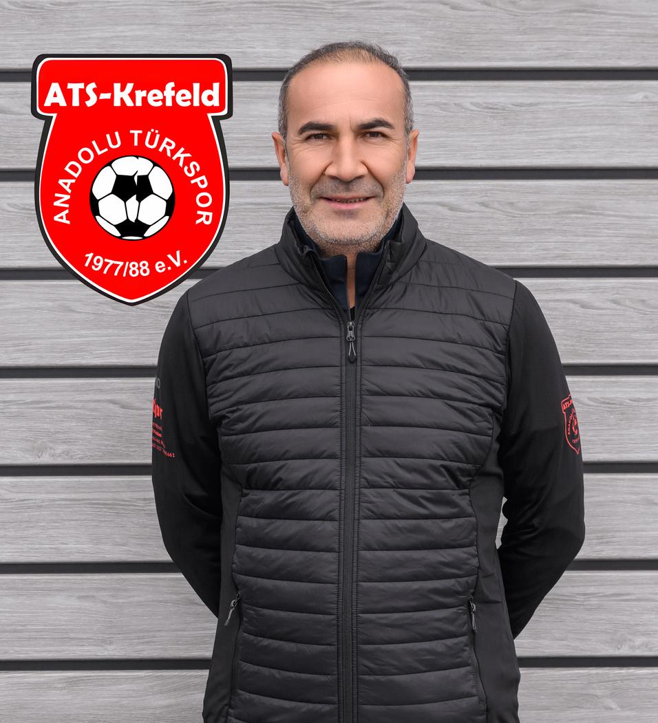 Mann mit kurzen Haaren und Jacke steht vor grauer Wand, das Logo von ATS Krefeld und Anadolu Türksport ist im Bild.