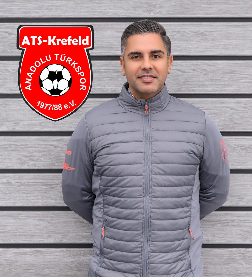 Mann in grauer Jacke steht vor einer Holzwand, neben dem Logo von ATS Krefeld und Anadolu Türkspor.